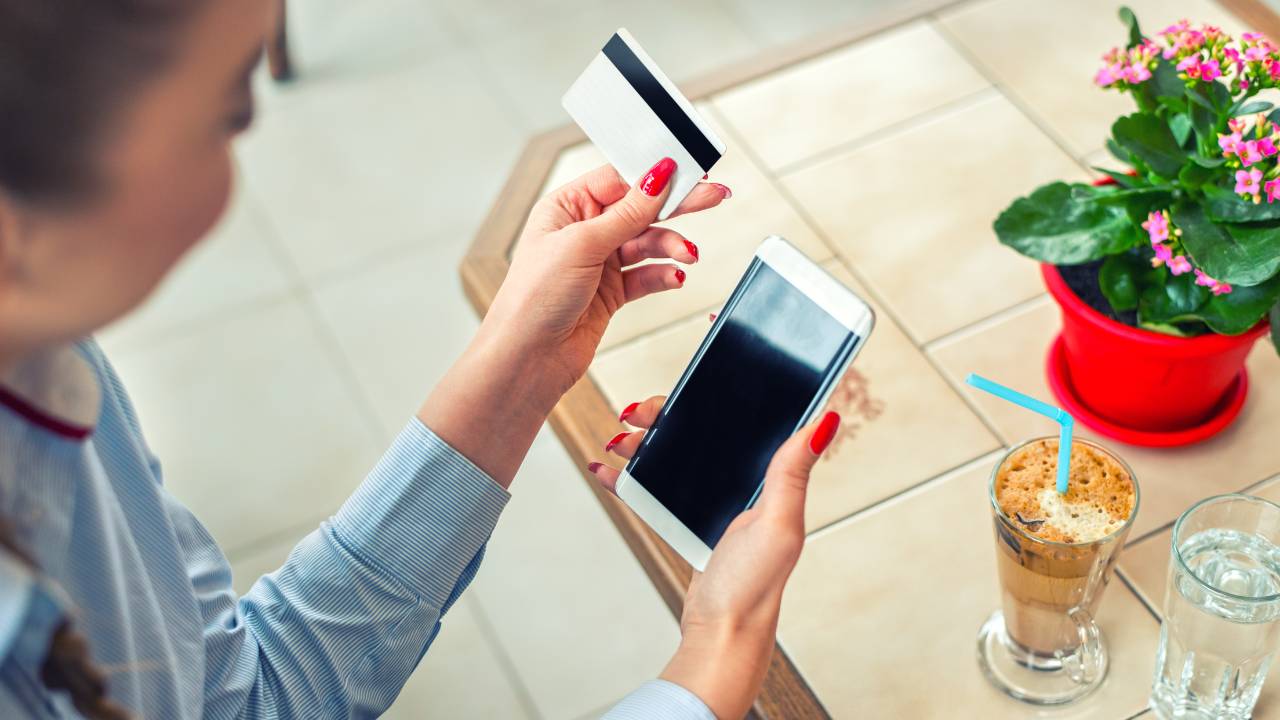 Mulher com um celular e um cartão de crédito em mãos