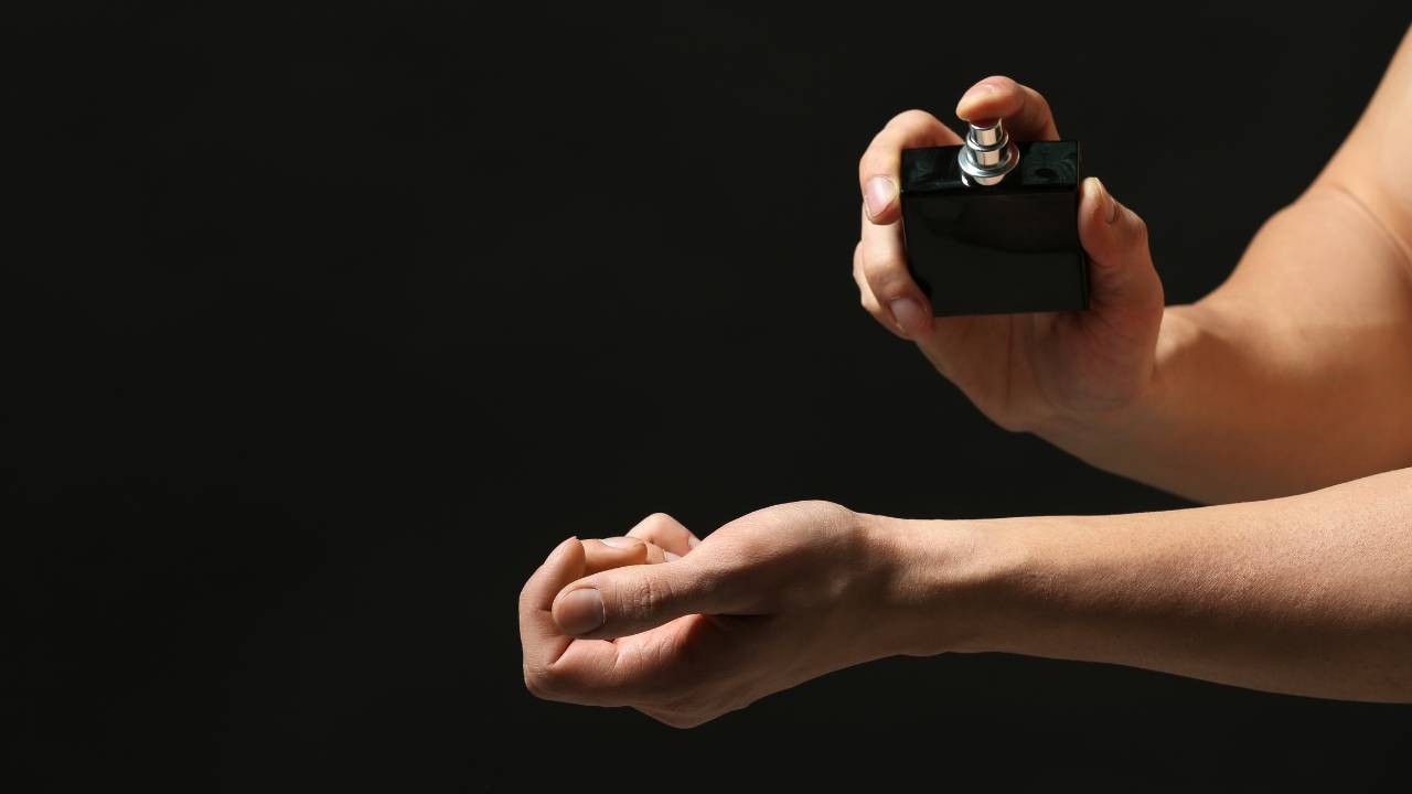 Um braço direito masculino aplicando perfume no braço esquerdo