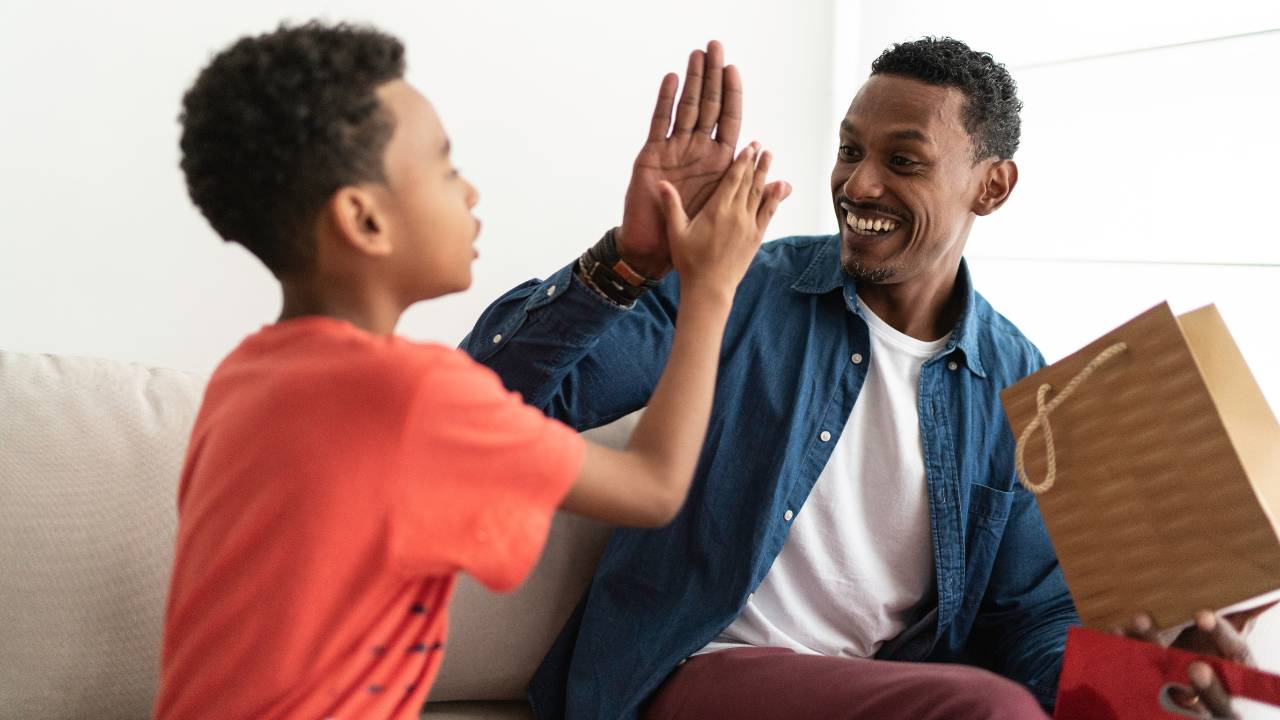 Homem negro recebendo um presente do filho pequeno; os dois celebram