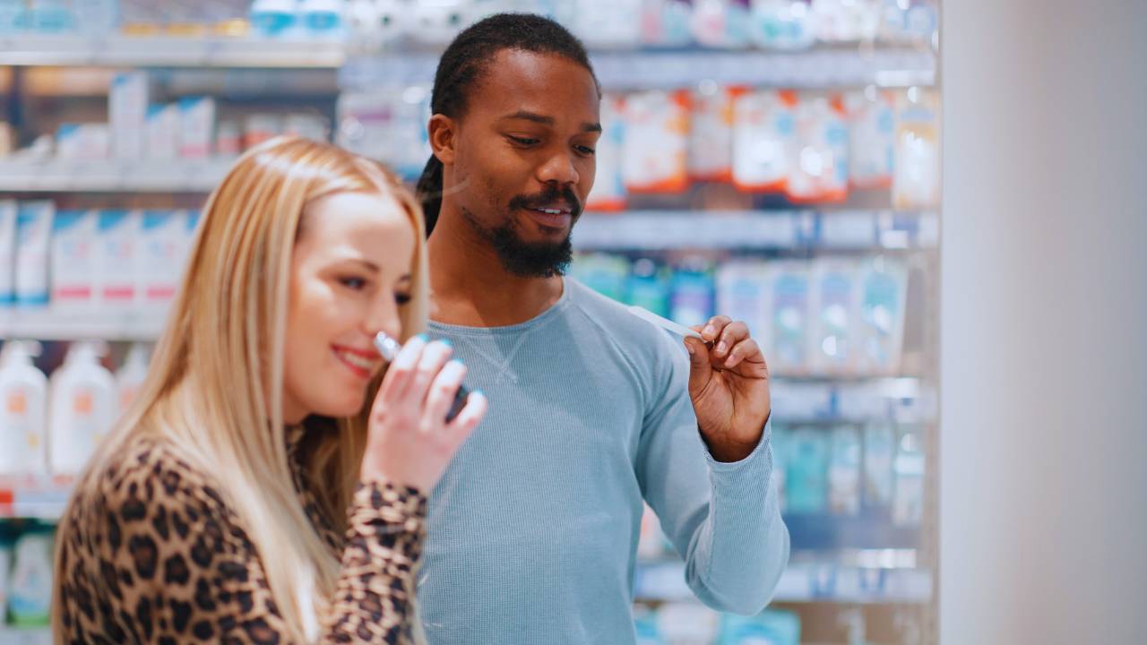 Mulher branca e homem negro provando perfumes em uma loja