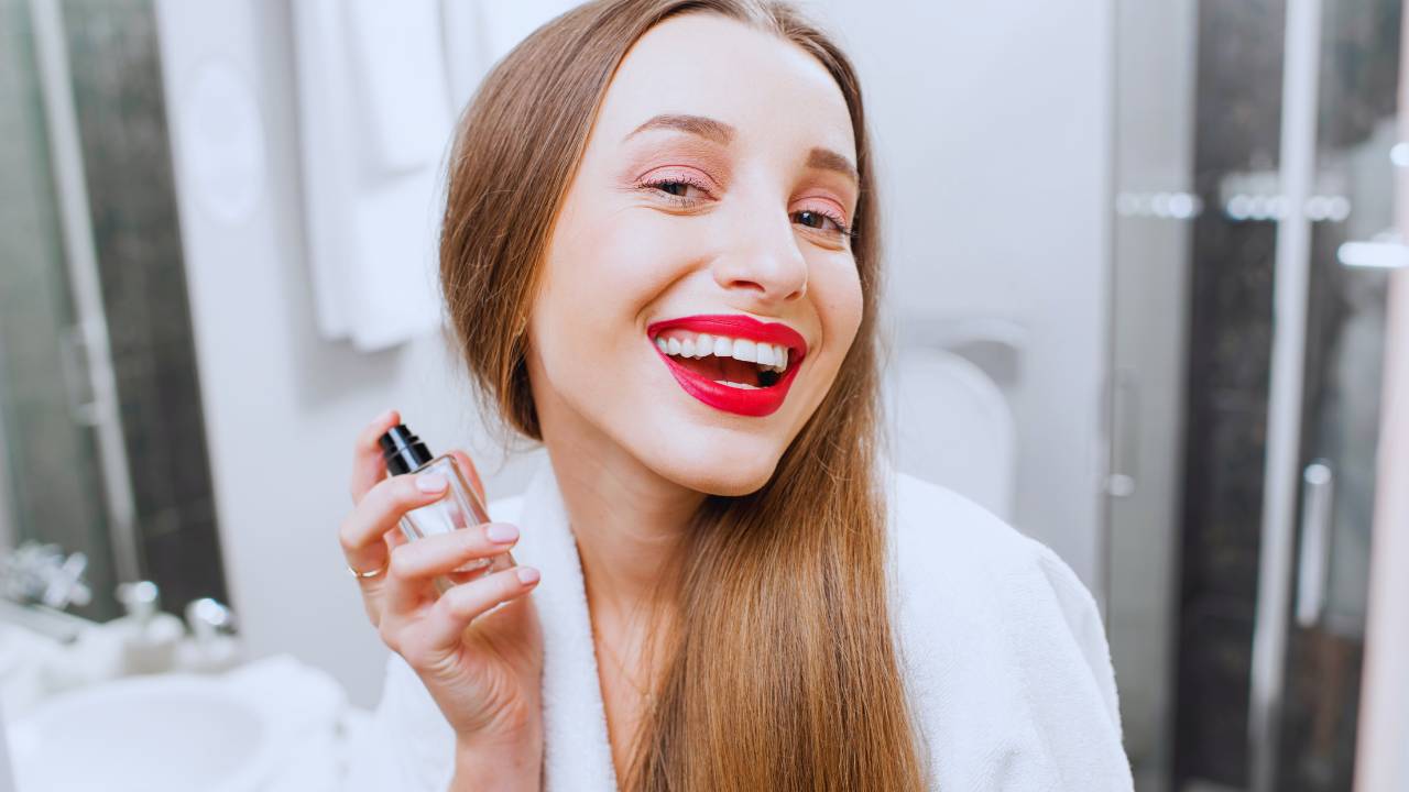 Mulher de cabelos compridos sorrindo para a câmera com um frasco de perfume na mão