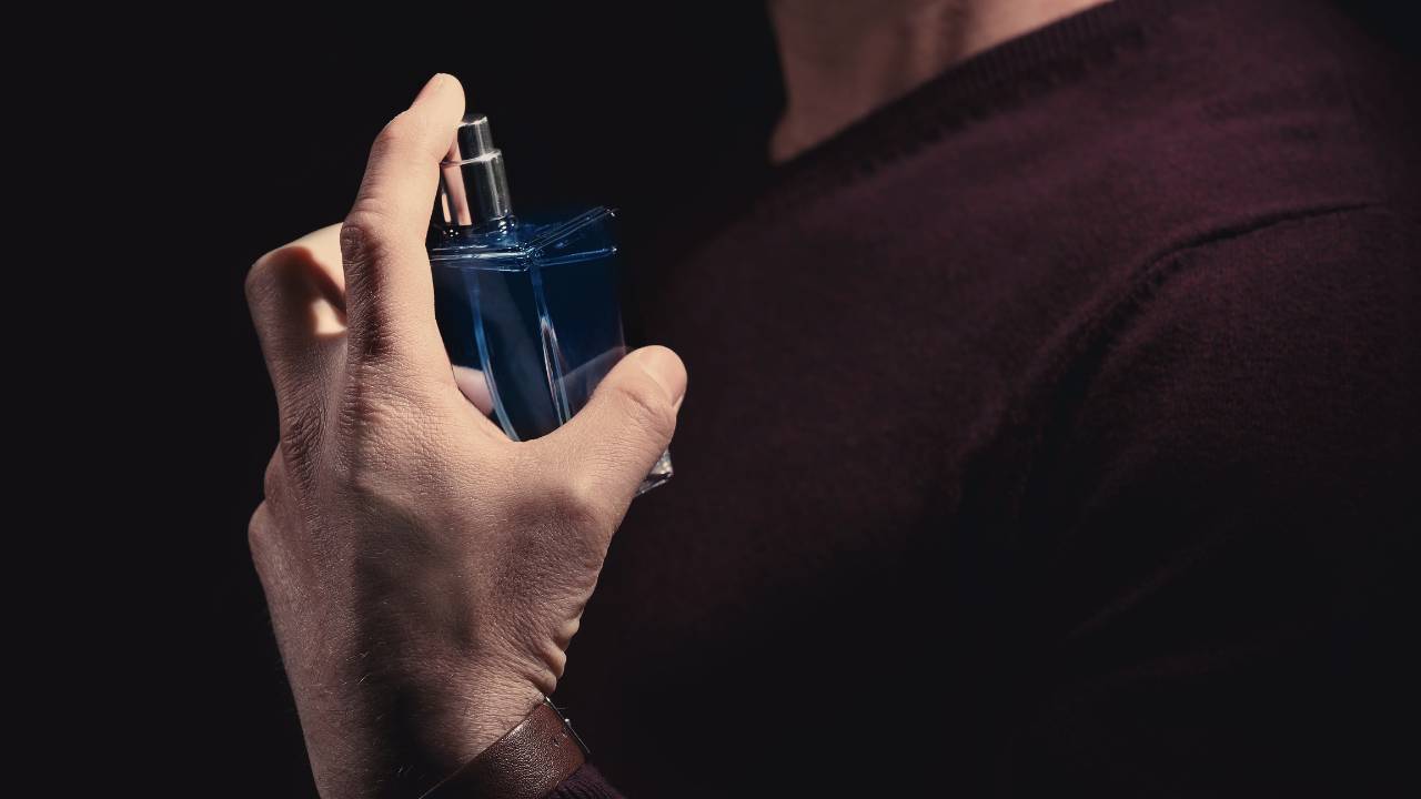 Homem de suéter cor de vinho espirra perfume no próprio pescoço