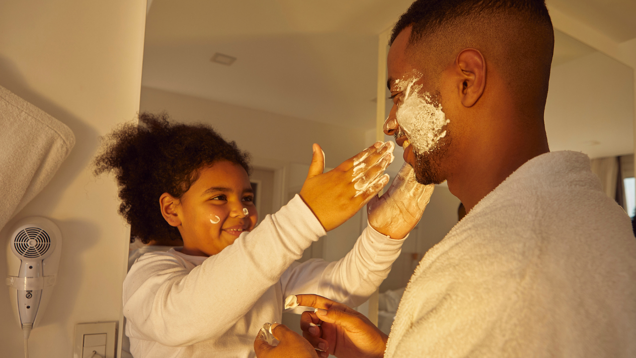 Homem negro brinca com sua filha, que espalha espuma de barbear em seu rosto