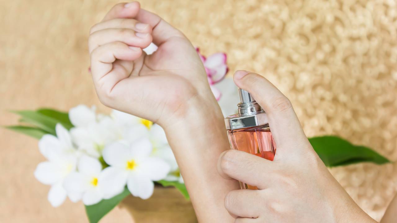 Close nos braços de uma mulher passando perfume no próprio pulso