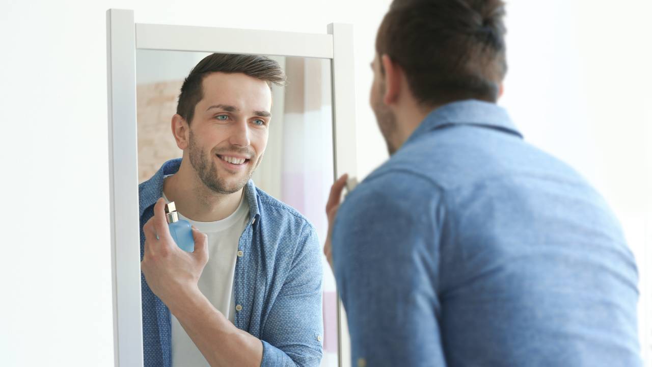 Homem branco se perfumando em frente a um espelho